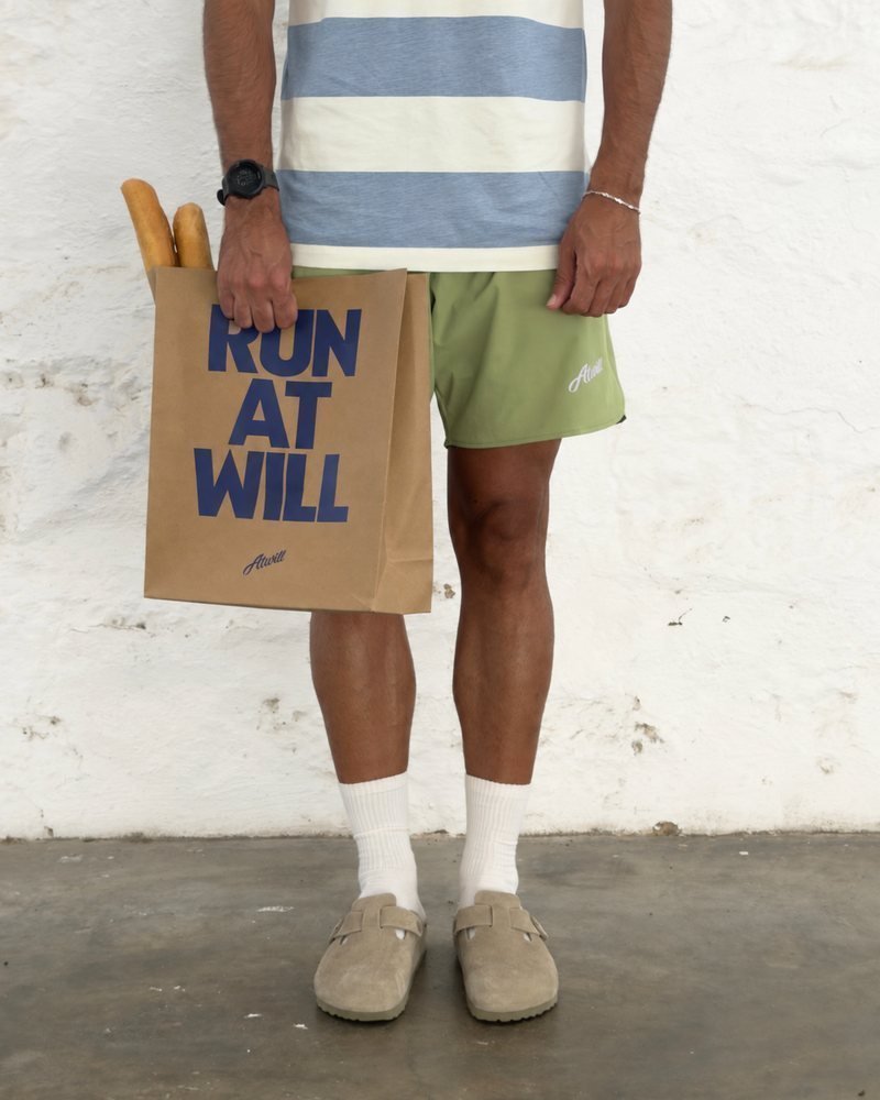 Runner in the Dusty Blue Ellis Tee and green East End Shorts holding a Run At Will bag with baguettes